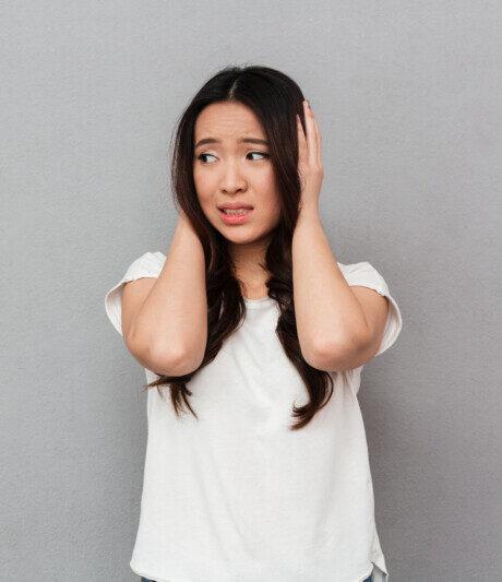 portrait asian puzzled woman 20s white t shirt touching her head looking aside confusion isolated gray wall e1743534974251