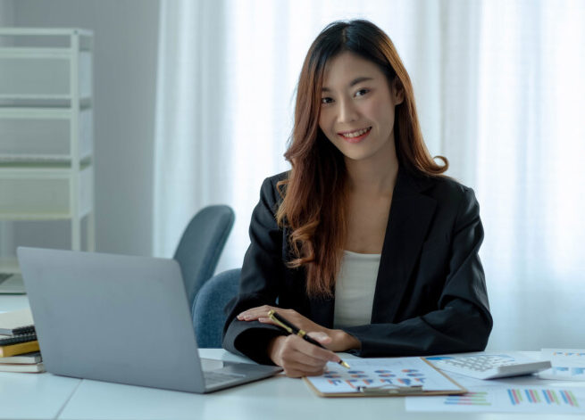 charming asian woman working office using laptop looking cameraxa e1747143465322
